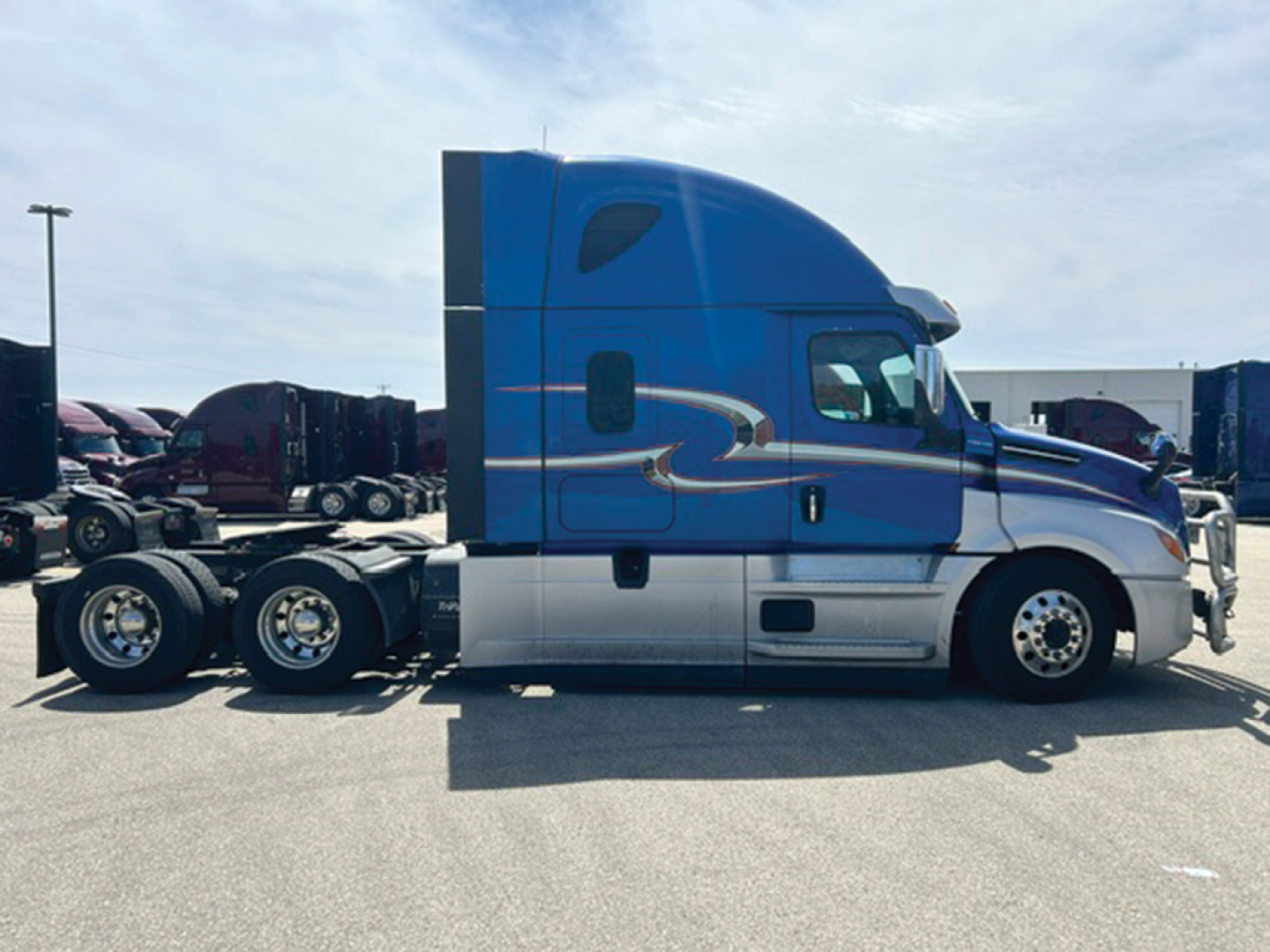 Truck cab side view showing blue Freightliner Cascadia126 sleeper with silver lower section and chrome wheels.