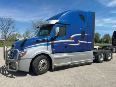Front-side view of a blue 2021 Freightliner Cascadia 126 sleeper tractor with chrome bumper guard and graphic decals.