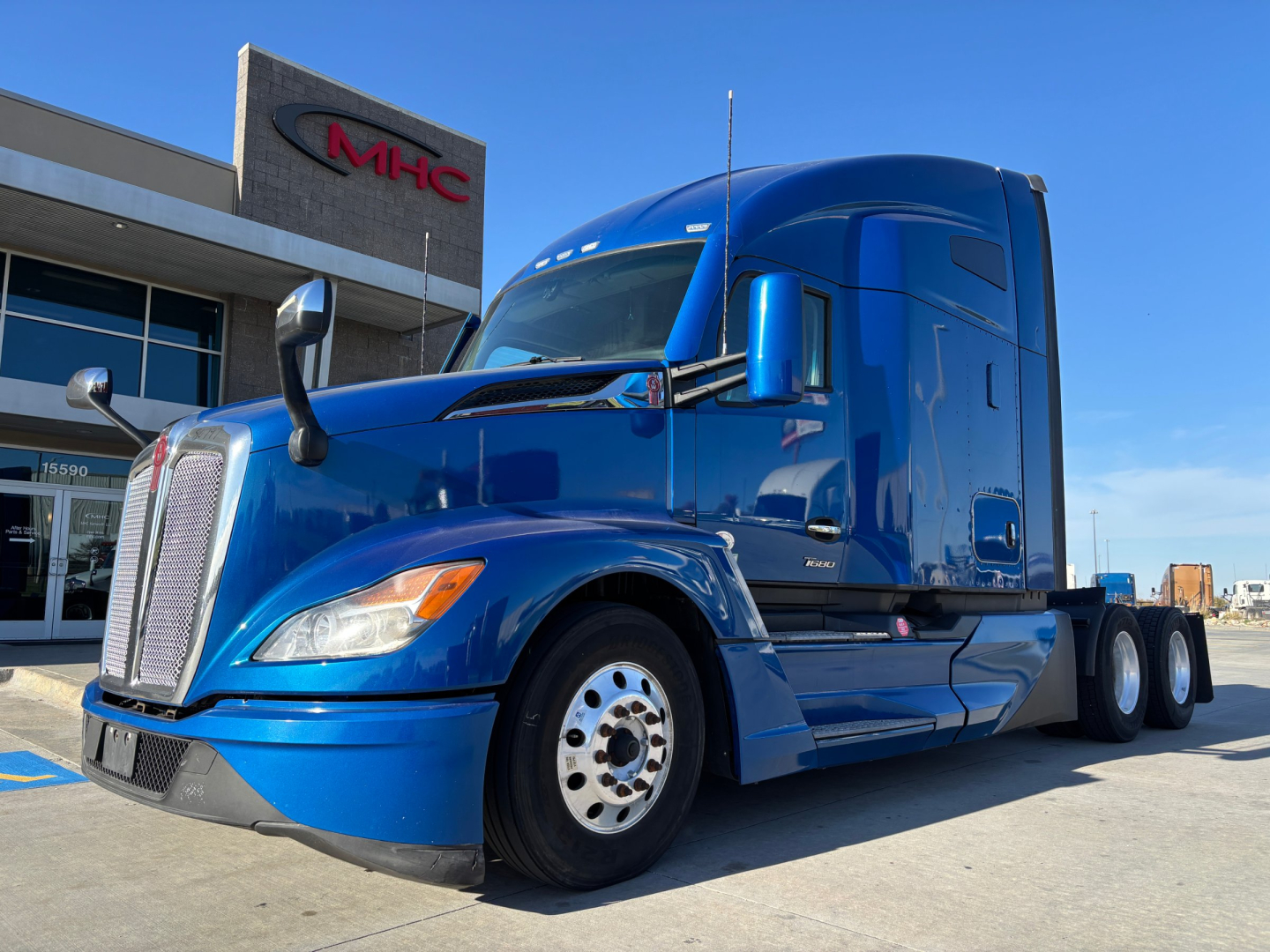 Kenworth T680 blue tractor-trailer viewed from front-right with sleeper cab, stock number 0632265 and dealership building in background.