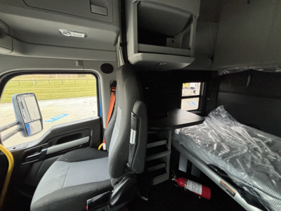 Kenworth T680 cab interior with sleeper area, overhead storage, and open cabinet; seat and dashboard visible.