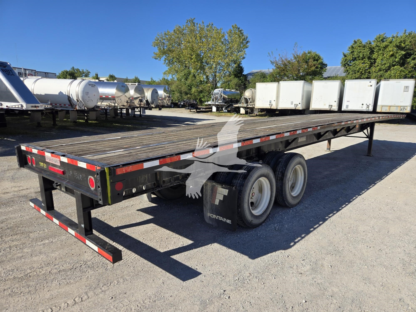 Flatbed trailer showing dual rear axles and wooden deck with diamond plate edge, Fontaine logo on mudflaps and rear bumper.