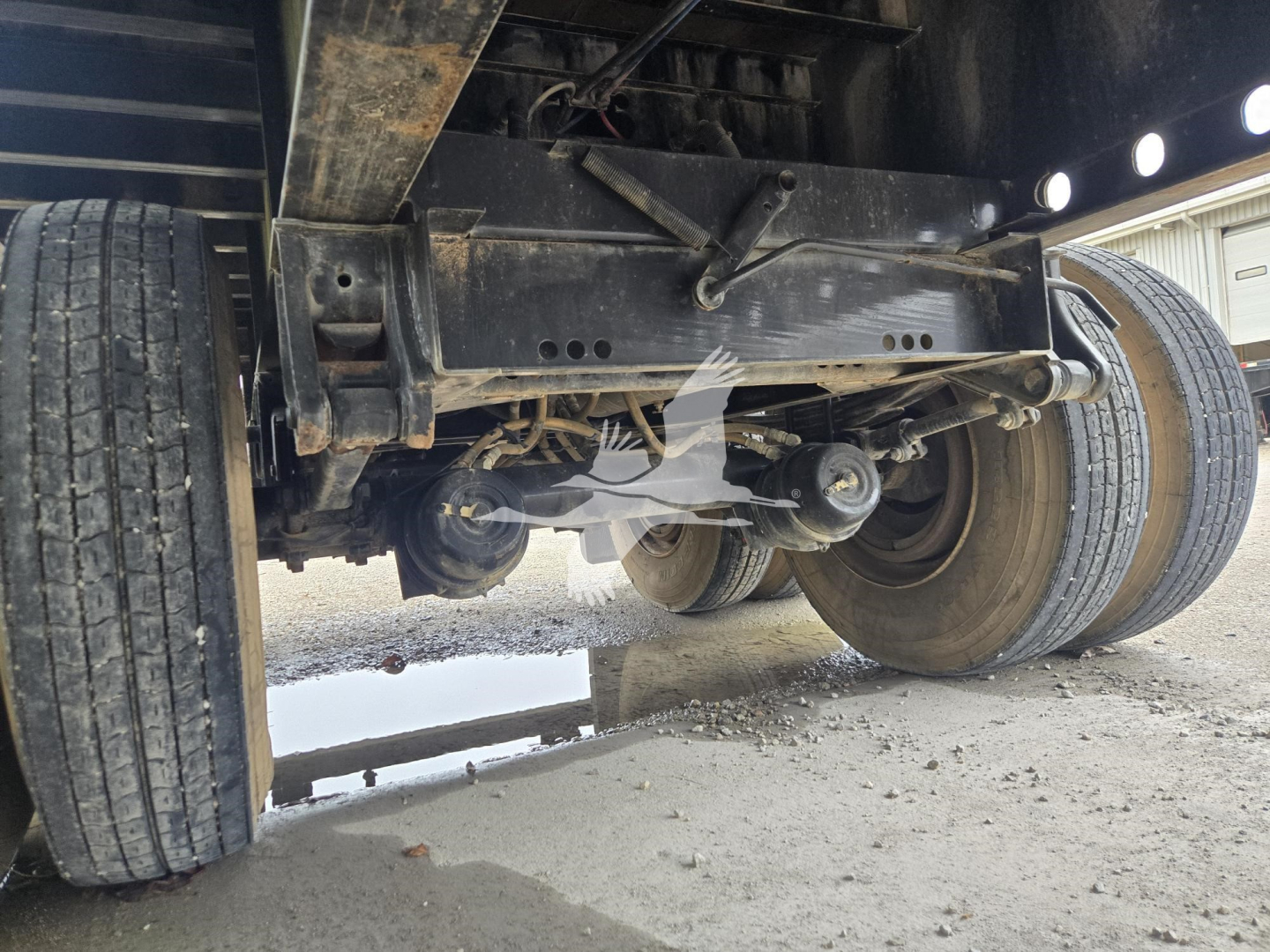 Sidelong view of a Fontaine steel flatbed trailer underside showing rear axle, suspension, and dual tires with undercarriage framing.