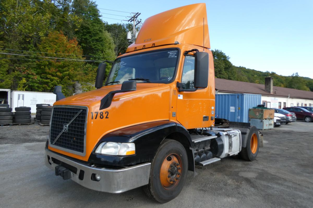 Orange Volvo VNM42T daycab truck shown from front-left angle with elevated cab and visible VIN placard; stock number 0924253 notations on truck.