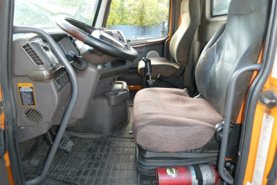Cab interior of a 2012 Volvo VNM42T variant showing driver seat, steering wheel, dashboard, and floor mat; orange exterior visible at door frame.