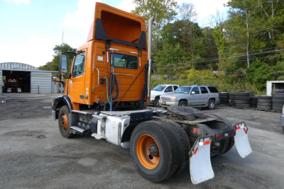 Truck rear/side view of a 2012 Volvo VNM42T daycab with orange cab, showing chassis, fifth wheel, and mud flaps.