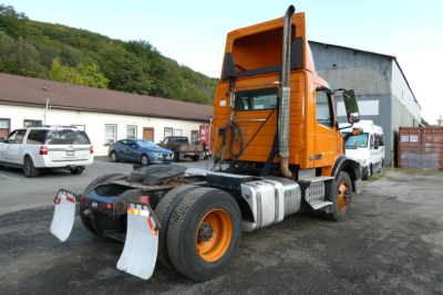 Front-right view of orange Volvo VNM truck with daycab configuration showing rear wheel area and lift equipment mounts.