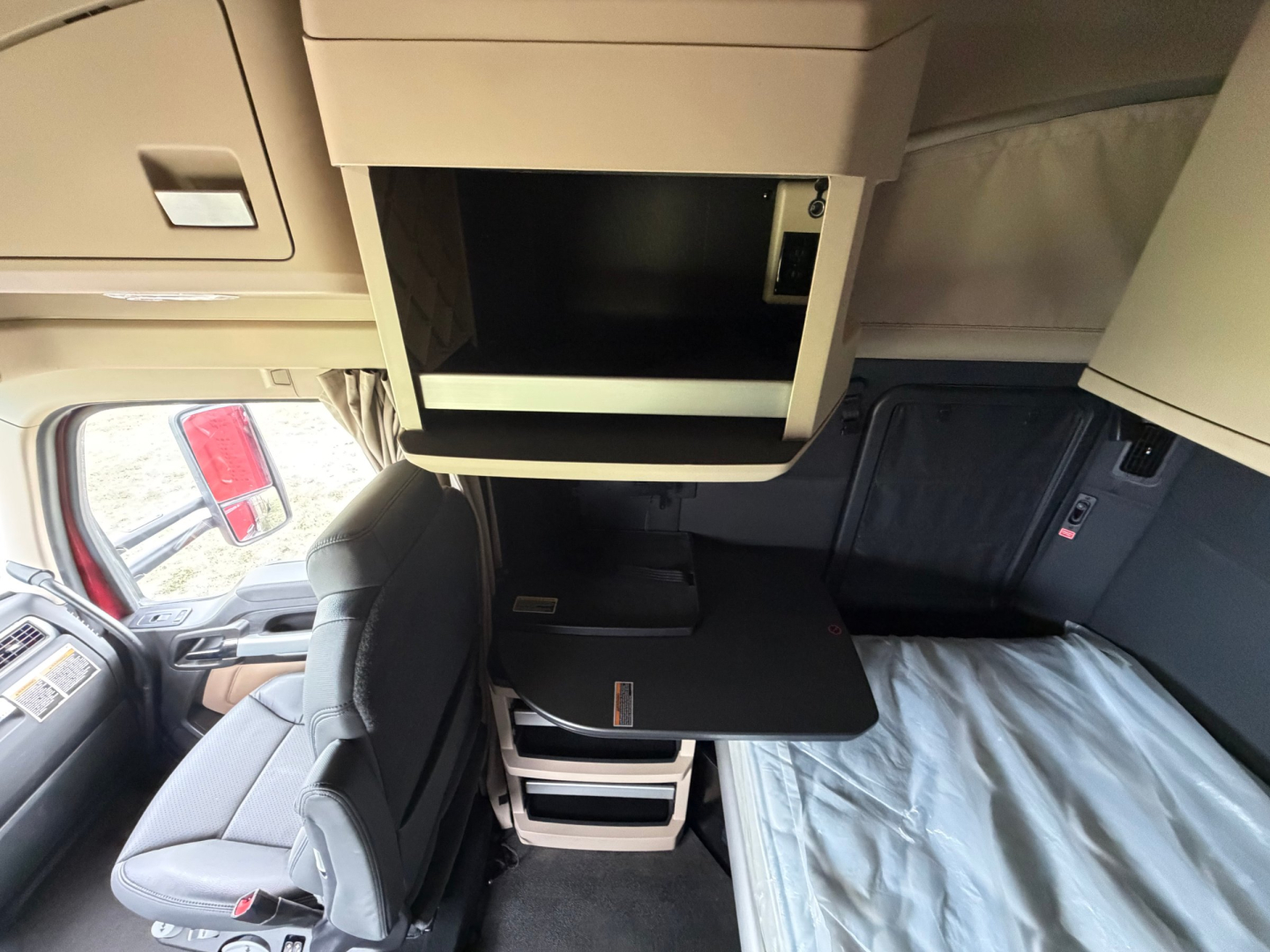 Kenworth T680 cab interior with sleeper area and overhead storage, showing seating and open shelves.