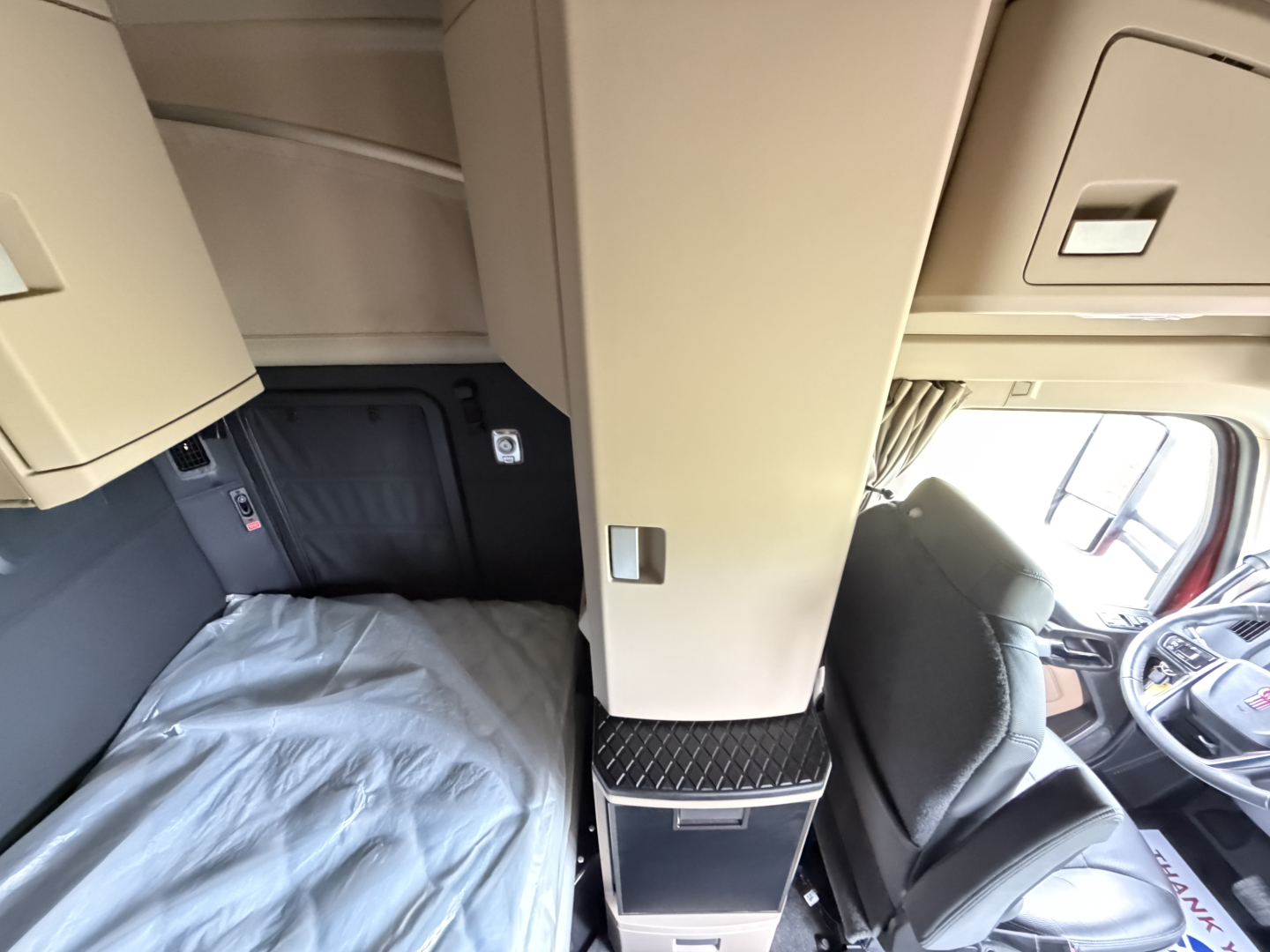 Kenworth T680 cab interior showing sleeper area and dashboard with beige panels and diamond-plate step; center console and storage compartments visible.