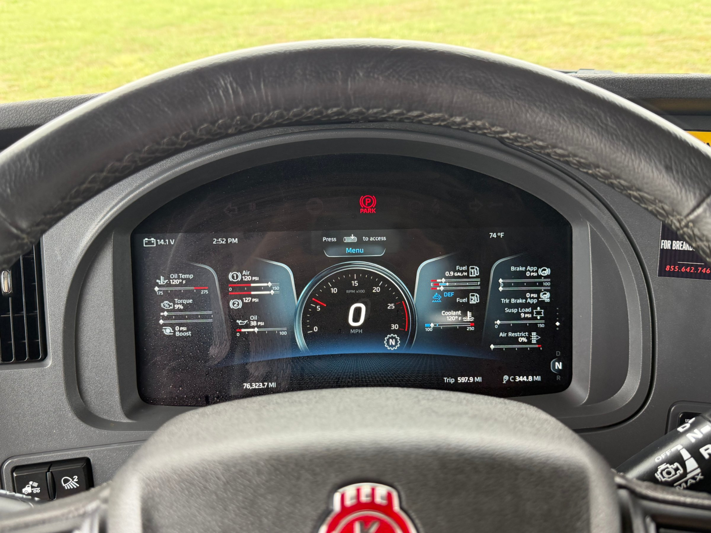 Kenworth T680 dash cluster view through steering wheel showing digital gauge display and warning icons.