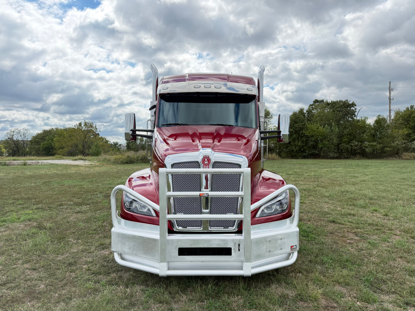 Kenworth T680 truck front view showing large chrome grille guard and bold headlights in a grassy area.