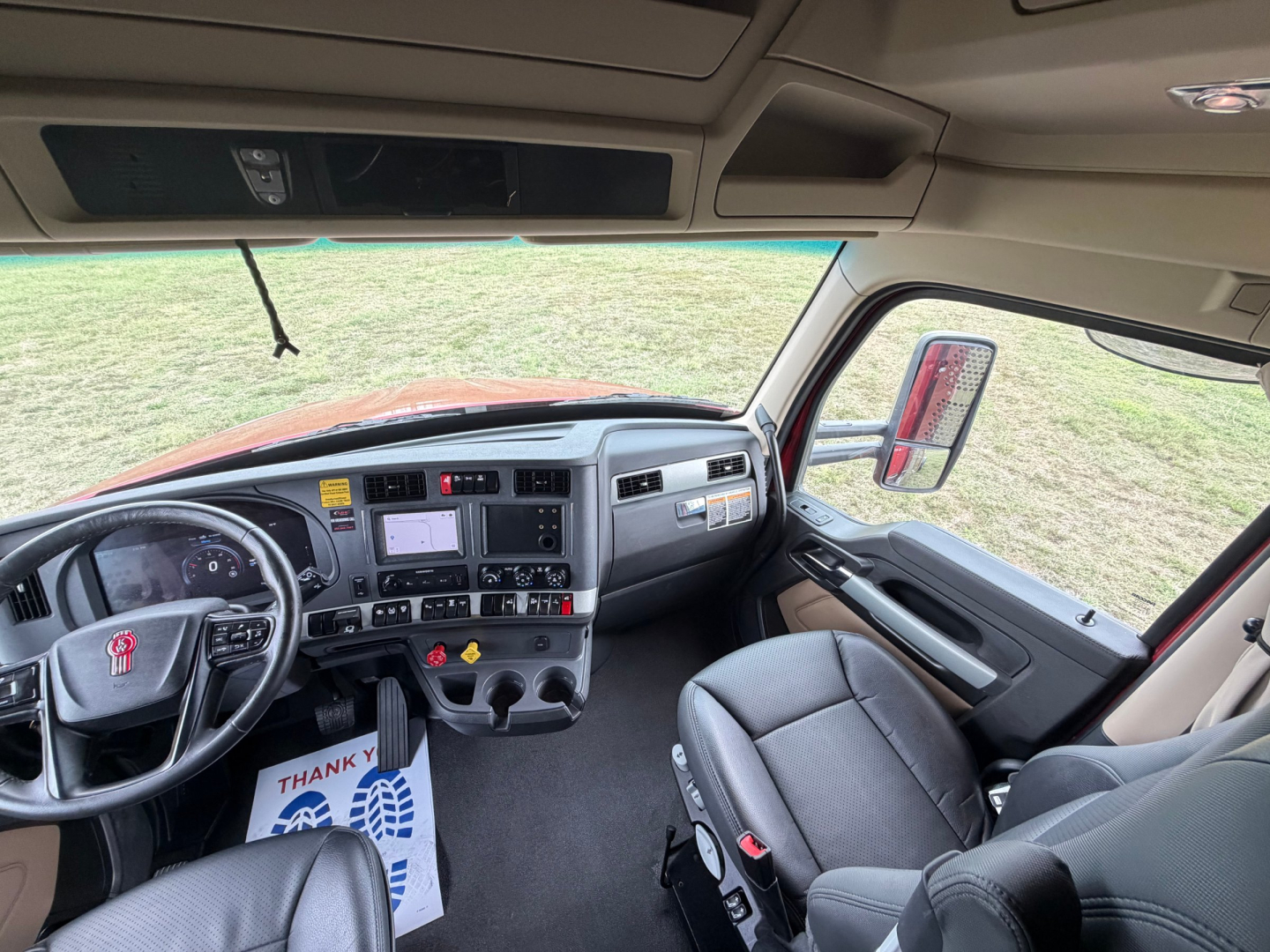 Kenworth T680 truck interior dashboard and steering wheel view from driver seat with grey seats and overhead storage.