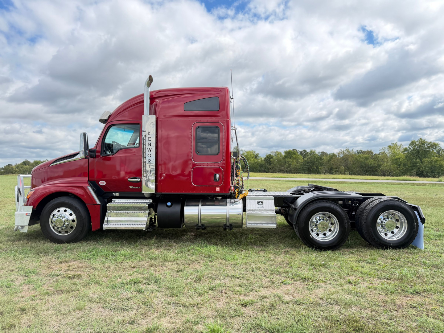 Kenworth T680 conventional sleeper truck side view showing red cab, chrome exhaust stack, dual rear wheels, and fuel tanks.