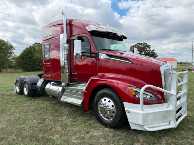 Kenworth T680 conventional sleeper truck in red with large chrome grille and white front bumper, side view showing dual rear axles and chrome fuel tanks.