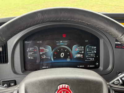 Kenworth T680 dash cluster view through steering wheel showing digital gauge display and warning icons.