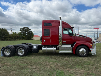 Kenworth T680 truck in red cab, side view showing fuel tanks, exhaust stack, and dual rear axles; no visible model text legible.