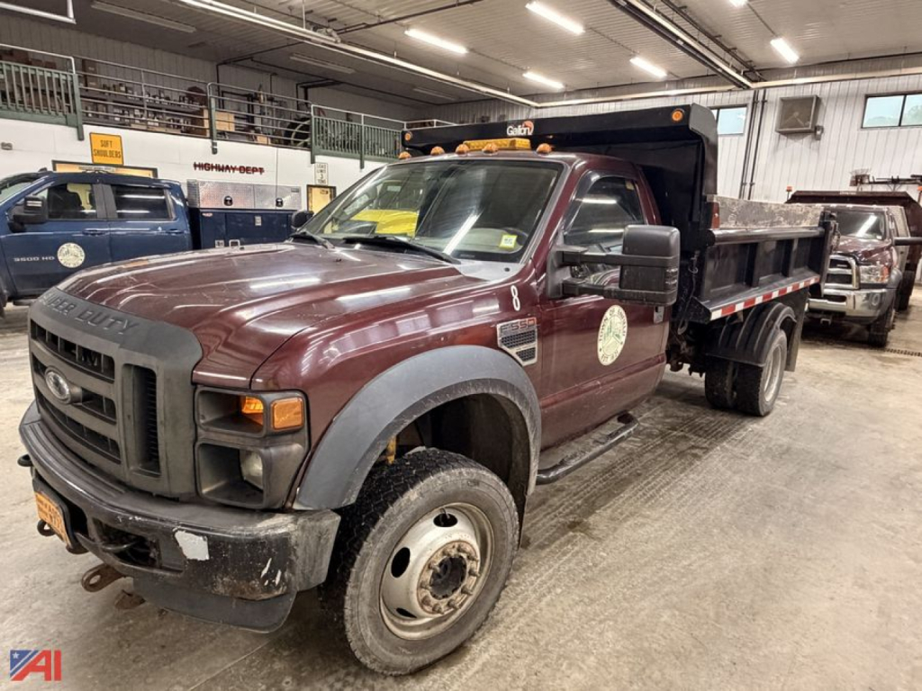 Ford F-550 Super Duty dump truck with plow in an indoor lot, front-left view showing black dump bed and dual rear wheels, maroon cab, plow mounts, daytime lights.