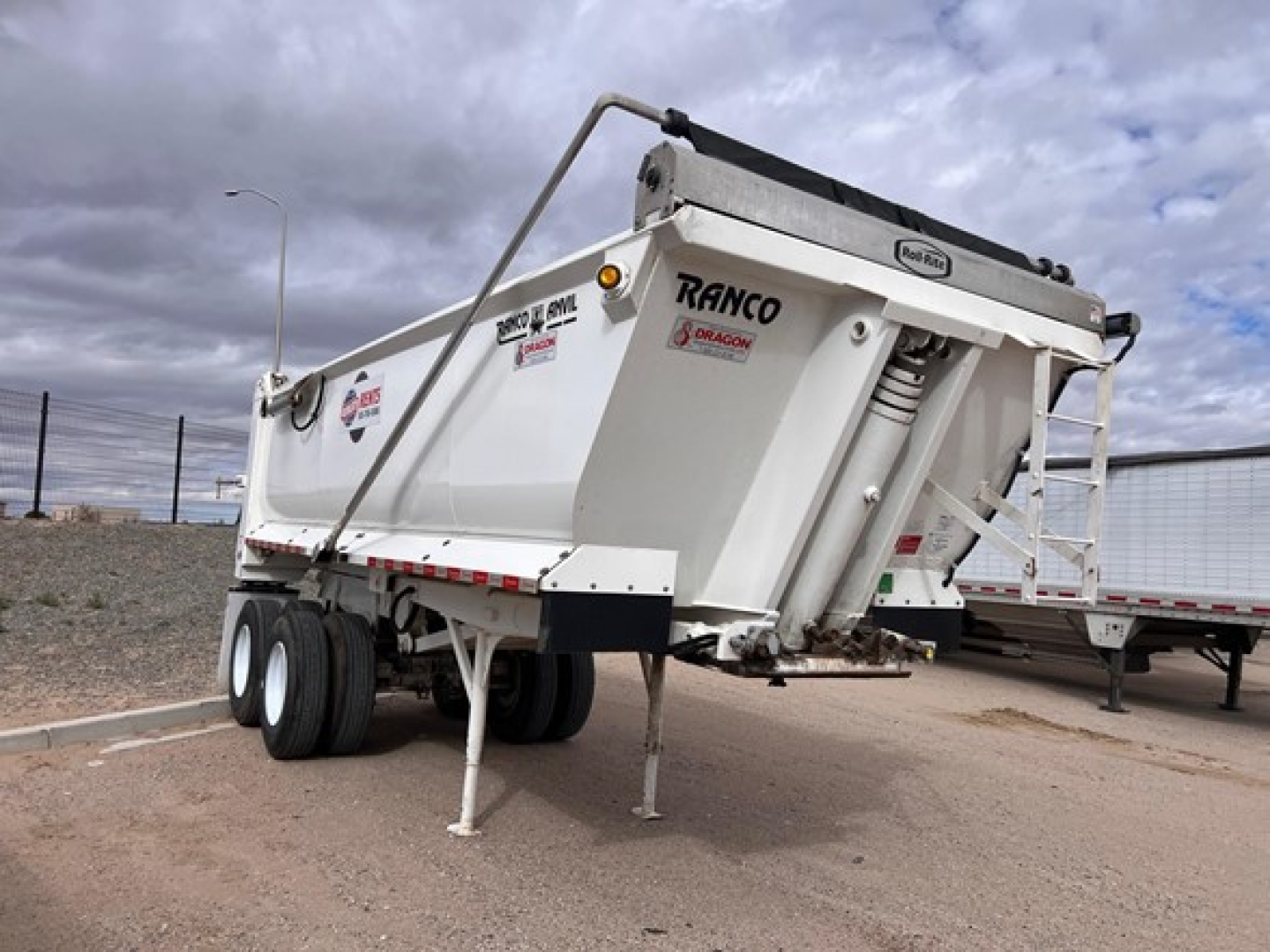 Ranco quarter frame steel end dump trailer viewed from side-right showing dual rear axles, hydraulic tailgate, and support legs with ramps folded on top.