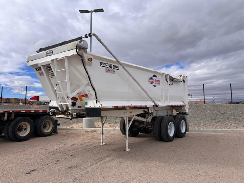 Quarter frame end dump trailer showing Ranco brand decals and model information on the side of a white steel trailer, with landing gear and wheels visible.