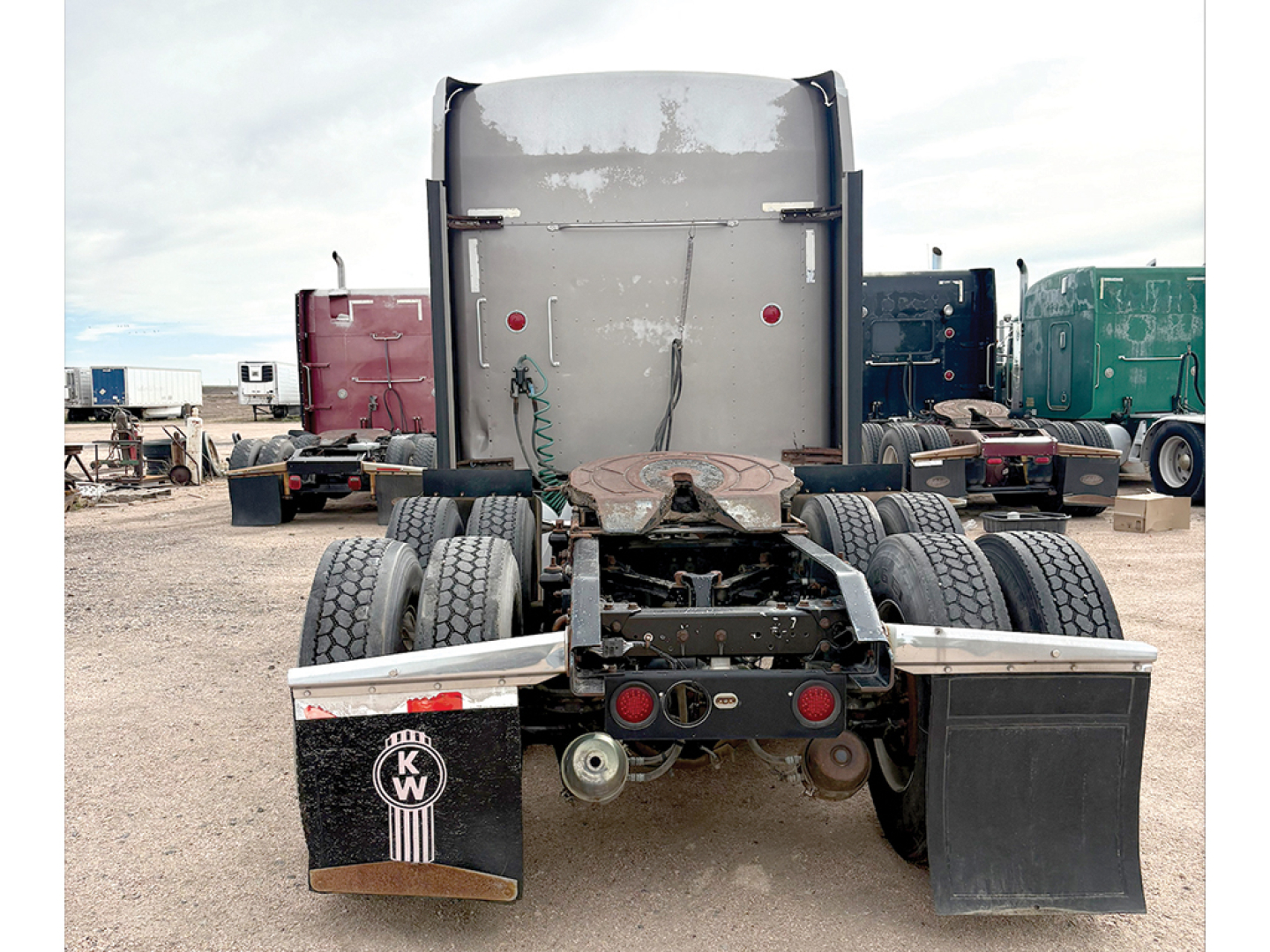 Kenworth W900L AeroCab tractor rear view showing dual rear axles, fifth wheel, mud flaps with KW logo, and exhaust components.