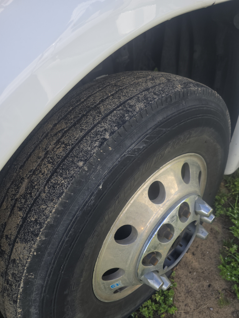 Truck wheel and front fender of a Freightliner Cascadia 125 showing front tire and polished steel wheel with multiple lug nuts.