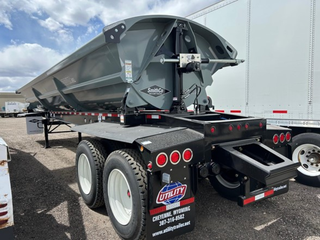 Side dump trailer in service with SmithCo air ride mechanism, dual rear axles, gray/black color, utility dealer plate area, VIN tag visible.