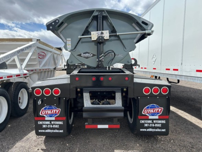 Rear view of a SmithCo air ride side dump trailer with red taillights and utility mud flaps in a yard.