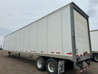 Trailer side view showing a white Wabash van trailer with dual rear axles, no visible branding, and reflective red-and-white tape along the bottom edge.
