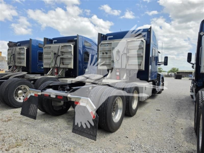 Kenworth T680 trucks in a lot, rear view showing dual rear axles and mud flaps with platform undercarriage.