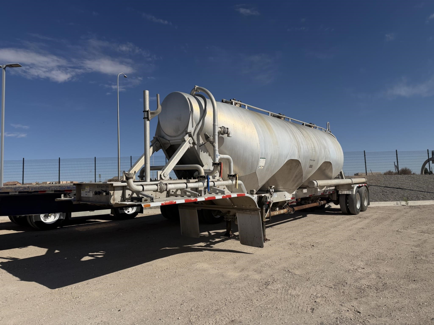 Pneumatic dry bulk trailer showing cylindrical tanker with hose reel and rear axle assembly.