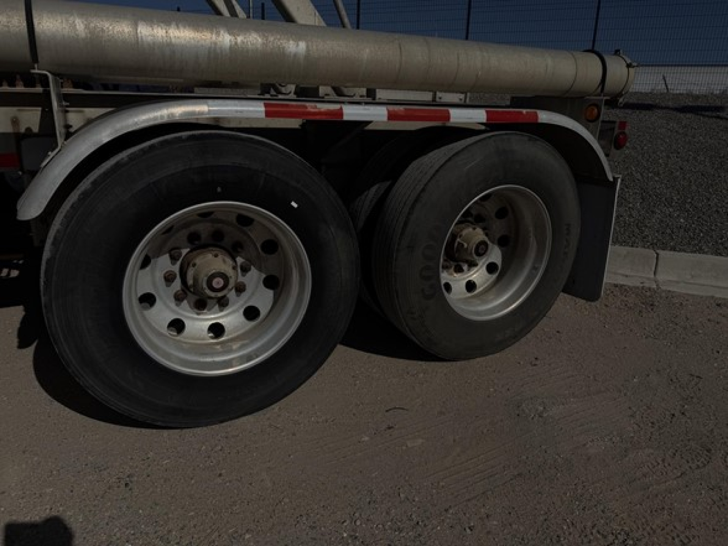 Pneumatic tank trailer wheels and dual-axle setup under trailer frame, showing tire treads and hub caps.