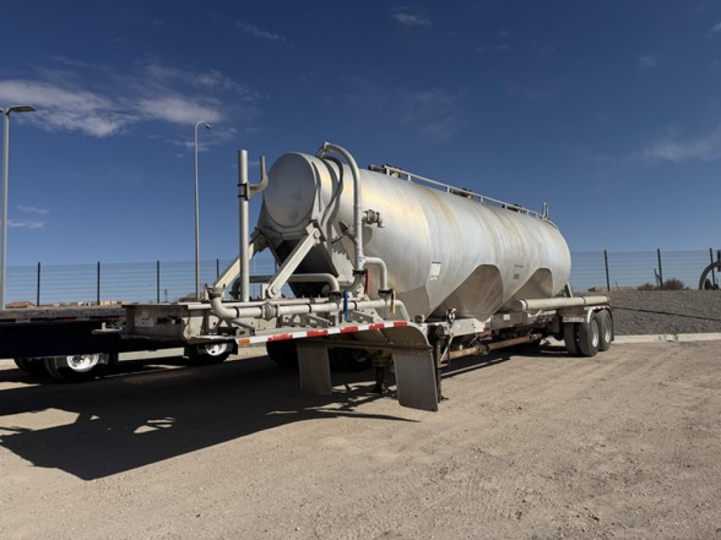 Pneumatic dry bulk tank trailer in service showing cylindrical aluminum tank on a dual-axle trailer with rear discharge and support legs.