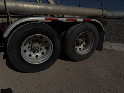 Pneumatic tank trailer wheels and dual-axle setup under trailer frame, showing tire treads and hub caps.