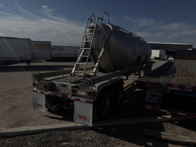 Pneumatic tank trailer in a yard showing rear view with ladder and dual axles.