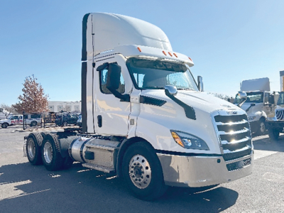 Truck cab showing 2021 Freightliner Cascadia 116 in white, side view with sleeper, six-wheel tractor, chrome front grille, daytime running lights, fuel tanks visible.