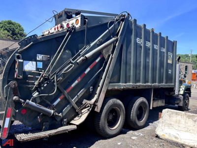 Dump truck rear and side view showing a large blue dump body with hydraulic mechanism and dual rear axles on a International 2654 Packer.