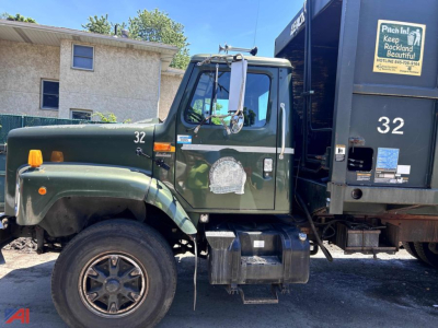 Truck cab and dump body from a 2001 International 2654 Packer in green, with number 32 on door and dump box, side steps, and a large black dump body.