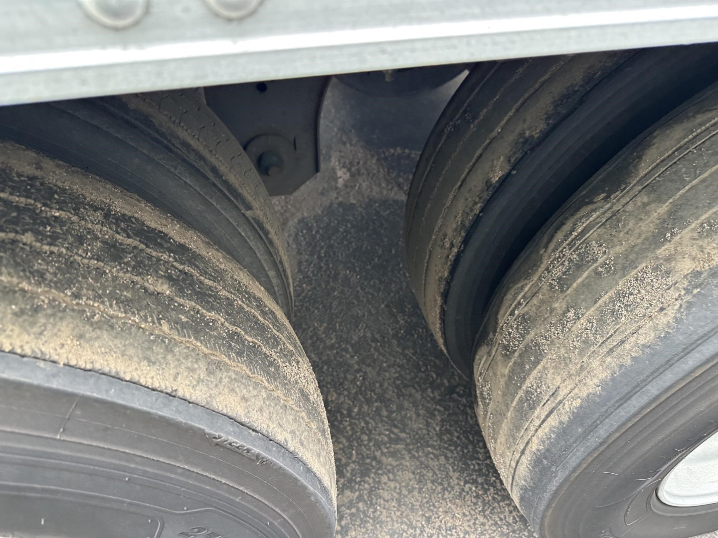Trailer dual tires showing dirty wheel hubs and mud on the tires; part of the reefer trailer body visible above.