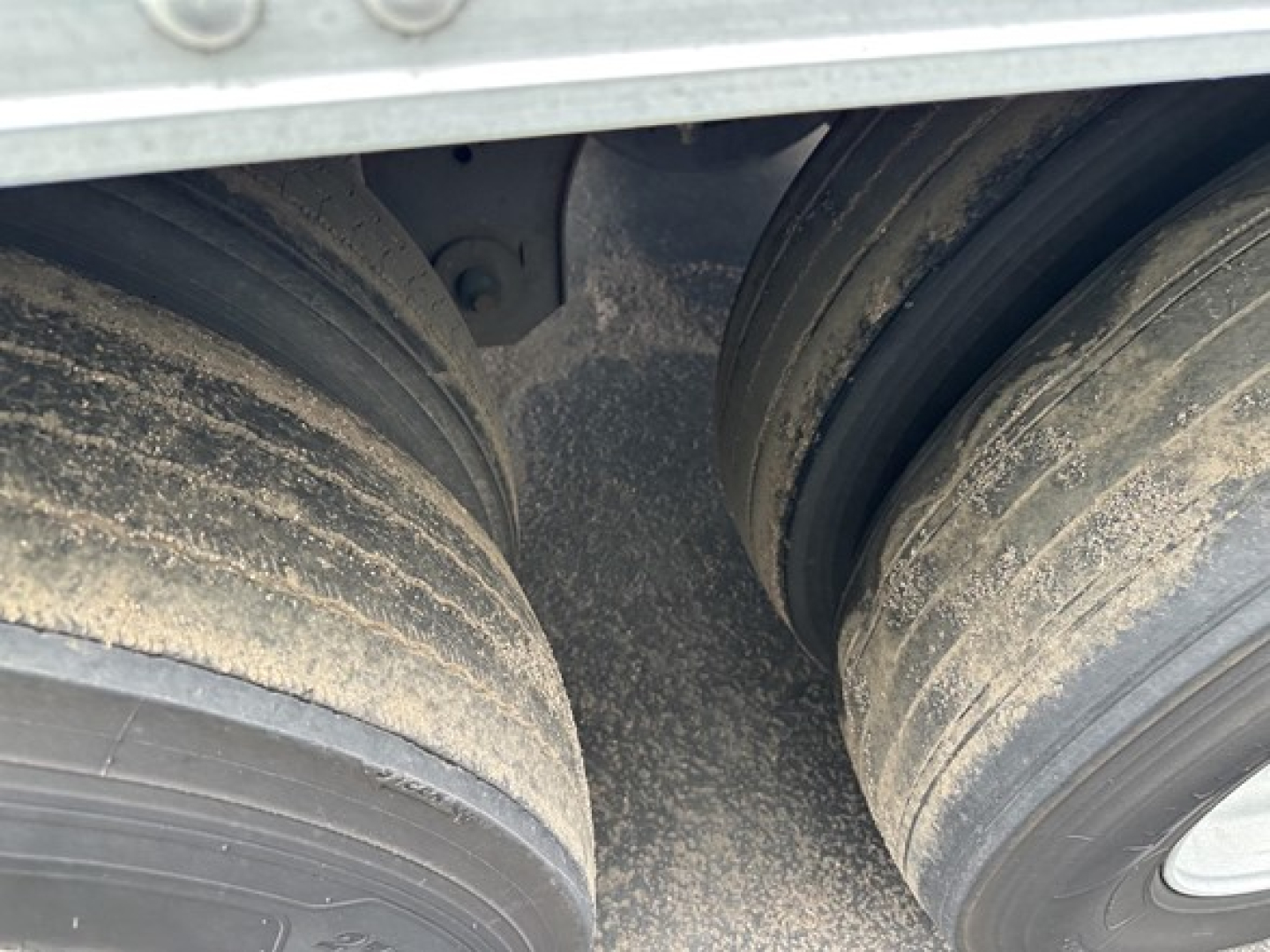 Trailer dual-axle wheels with dirt/residue on tires and frame seen from gap between axles.