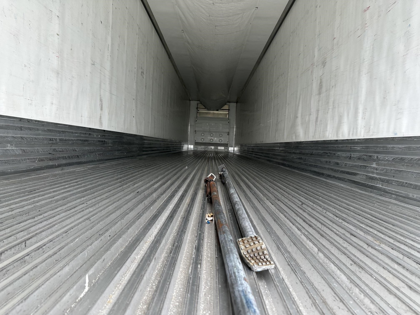 Utility 3000R trailer interior with ribbed floor, showing stacked metal components and tie-downs along the center, long empty cargo area.