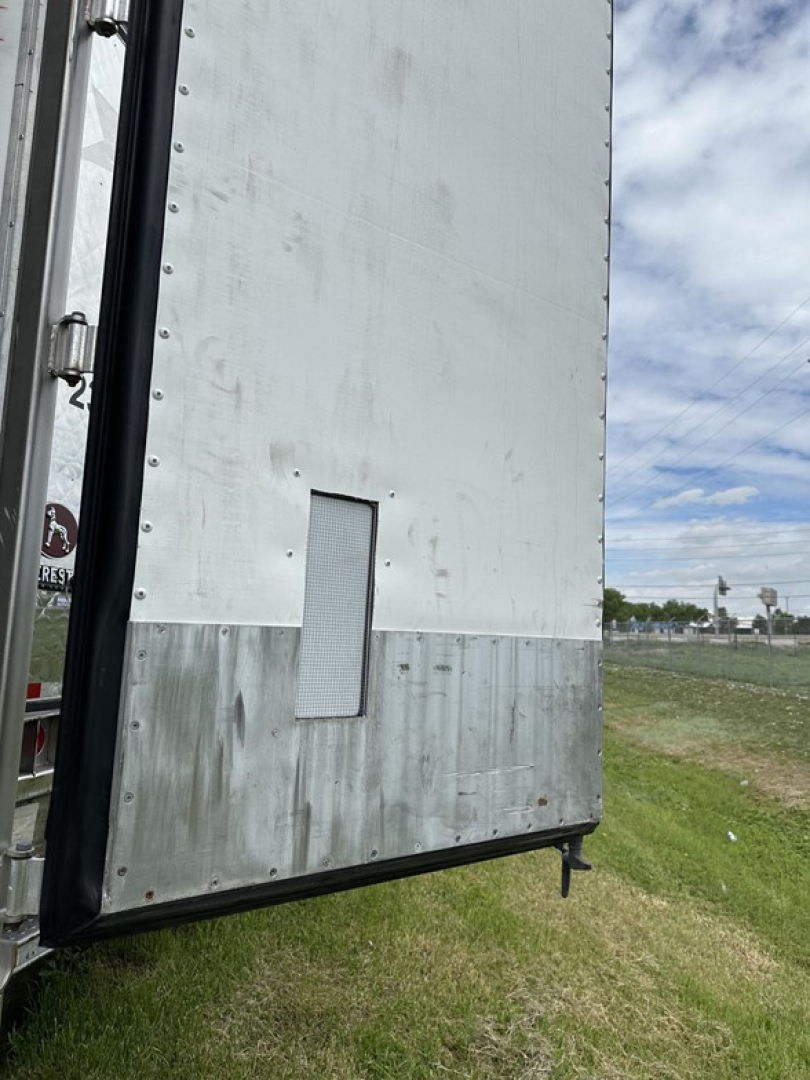 Rear of a utility 3000R reefer trailer with white upper panel and aluminum lower runner, small rectangular vent on door, grassy lot background.