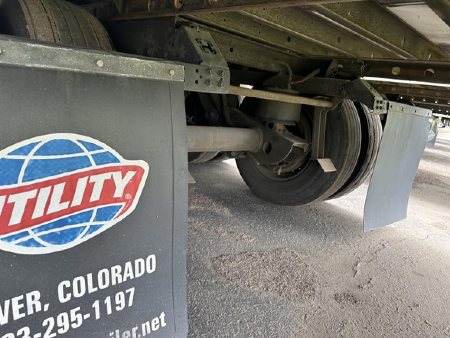 Trailer undercarriage with spare wheel, frame, and Utility logo on mudflap; faint text includes Denver, Colorado and phone number, and a metal fender.