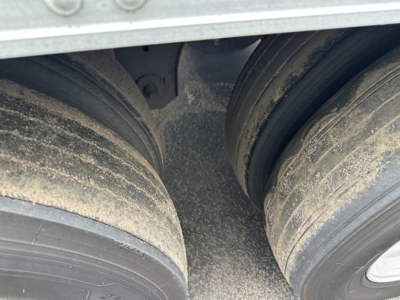 Trailer dual-axle wheels with dirt/residue on tires and frame seen from gap between axles.