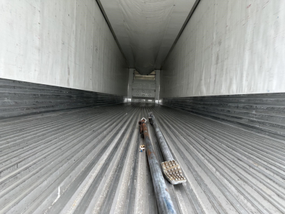 Utility 3000R trailer interior with ribbed floor, showing stacked metal components and tie-downs along the center, long empty cargo area.