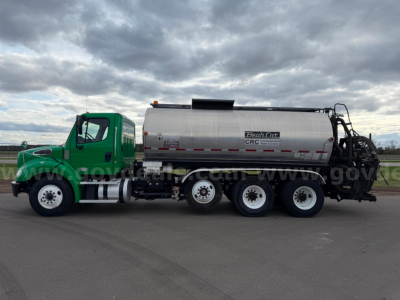 Freightliner Bearcat asphalt haul truck with a large stainless tank, green cab, three rear axles, and equipment at the back.