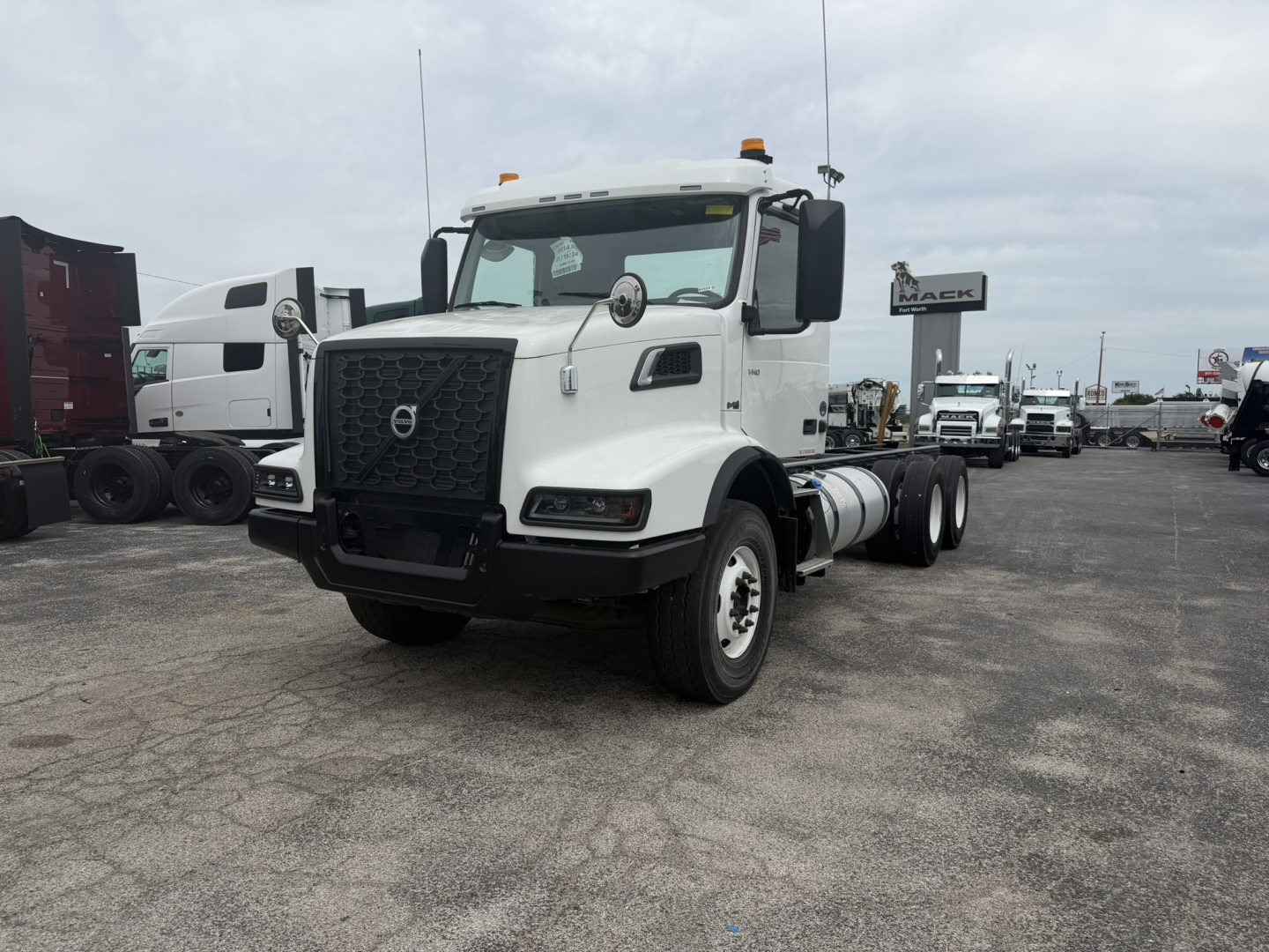 Volvo VHD86B300 cab and chassis truck viewed from driver front side showing front grille, headlights, and side mirrors; wheelbase and dual rear axles visible; stock lot background.