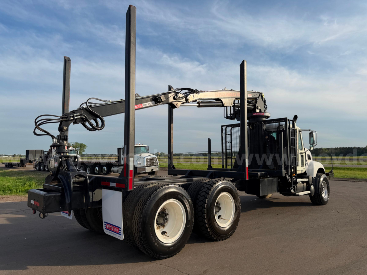 2007 Mack CV713 dump truck with grapple system and tall vertical supports, side view showing dual rear axles and crane arm.