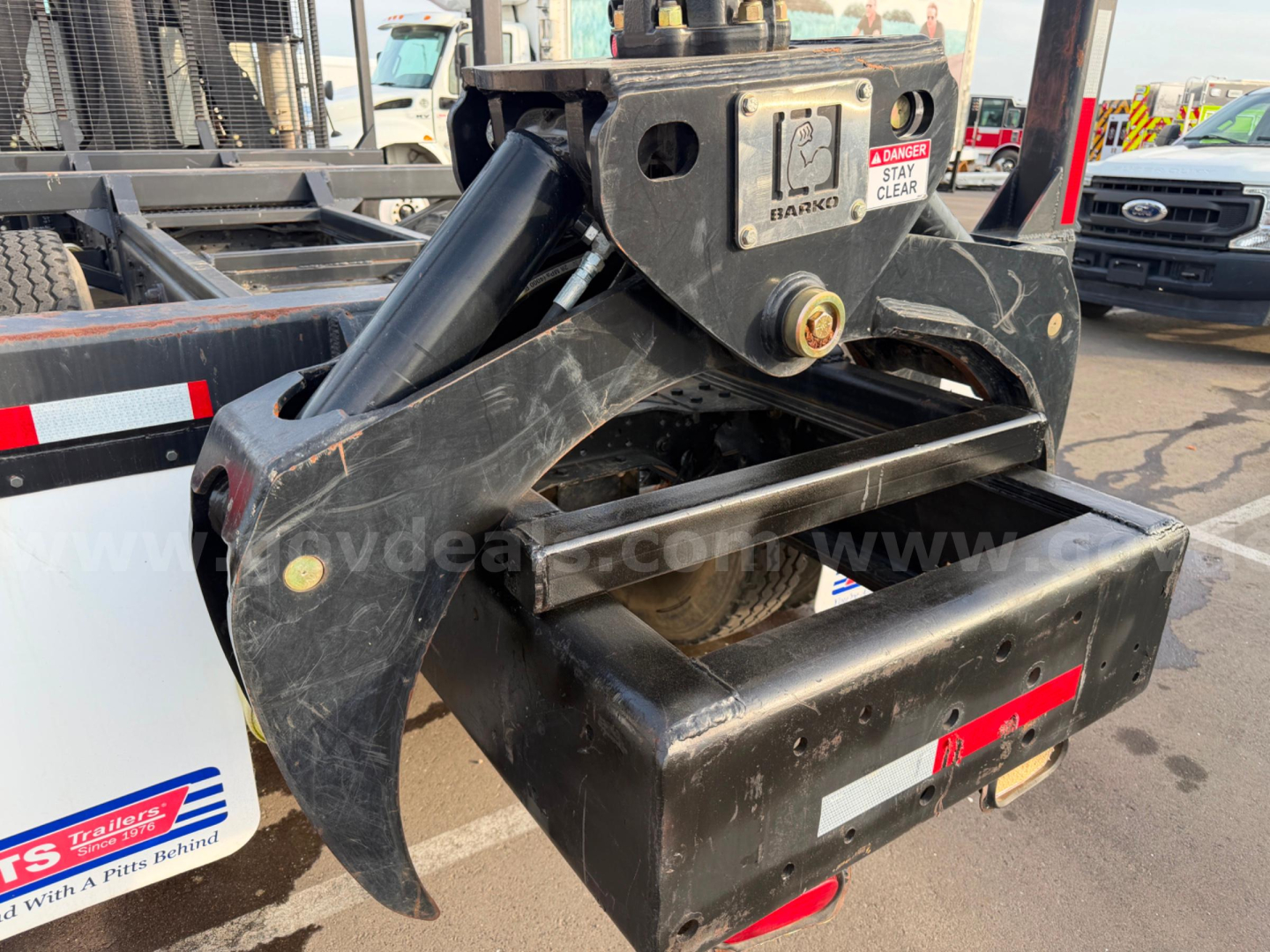 Mack CV713 grapple attachment showing hydraulic link and mounting hardware with warning labels.