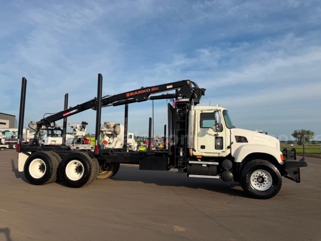 Mack CV713 heavy truck in side view with grappling crane boom and carrier, white cab, black equipment, multiple vertical stakes on the trailer chassis.