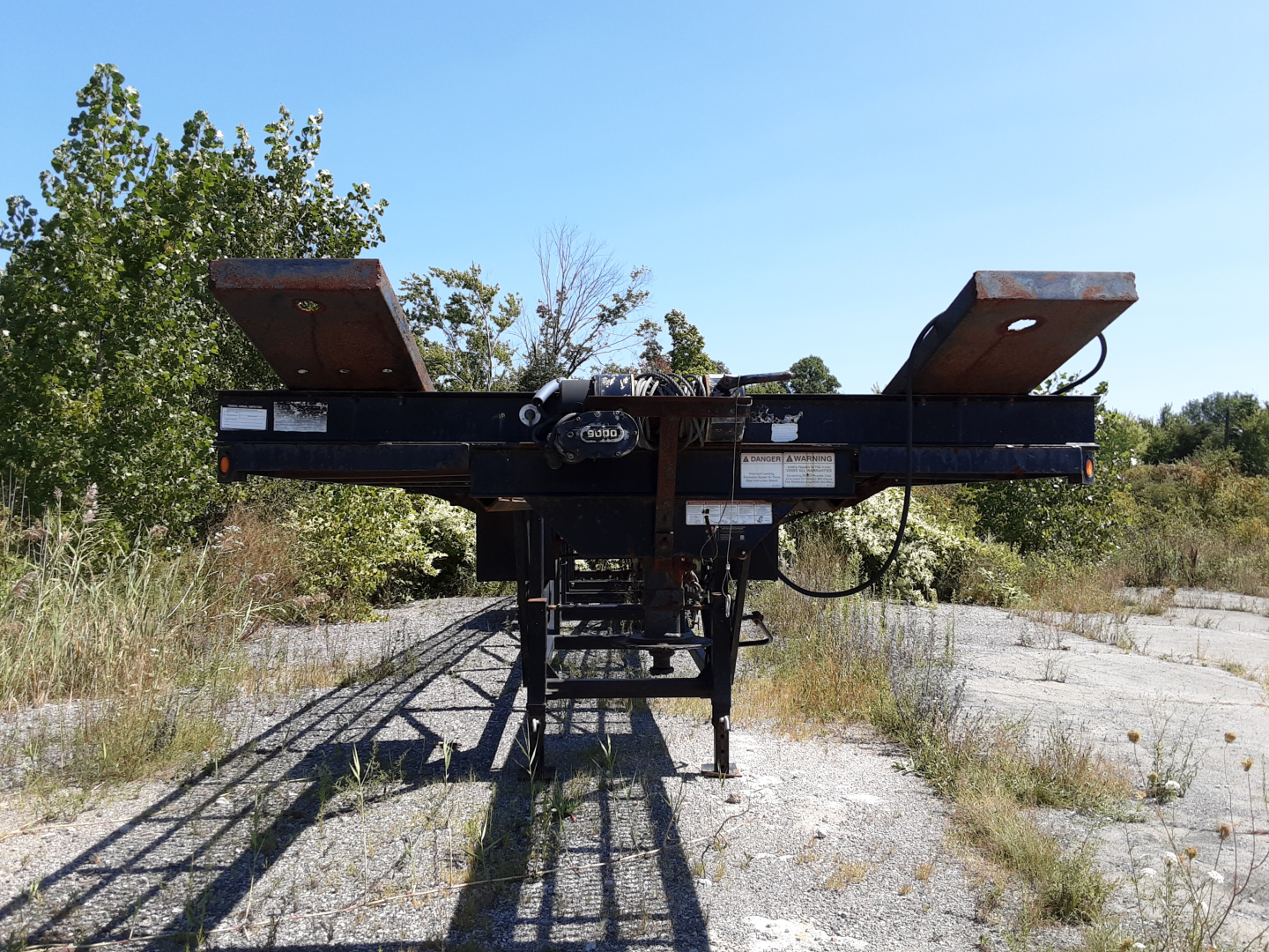 Trailer hitch platform of a Kaufman 3 car hauler viewed from rear, with ramps extended upward, showing metal frame and winch components.