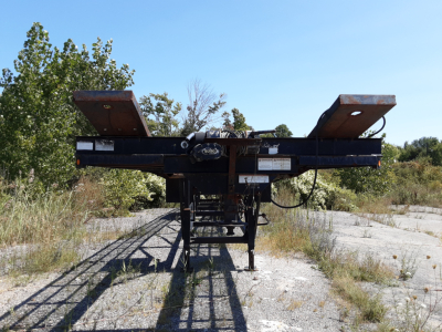 Trailer hitch platform of a Kaufman 3 car hauler viewed from rear, with ramps extended upward, showing metal frame and winch components.